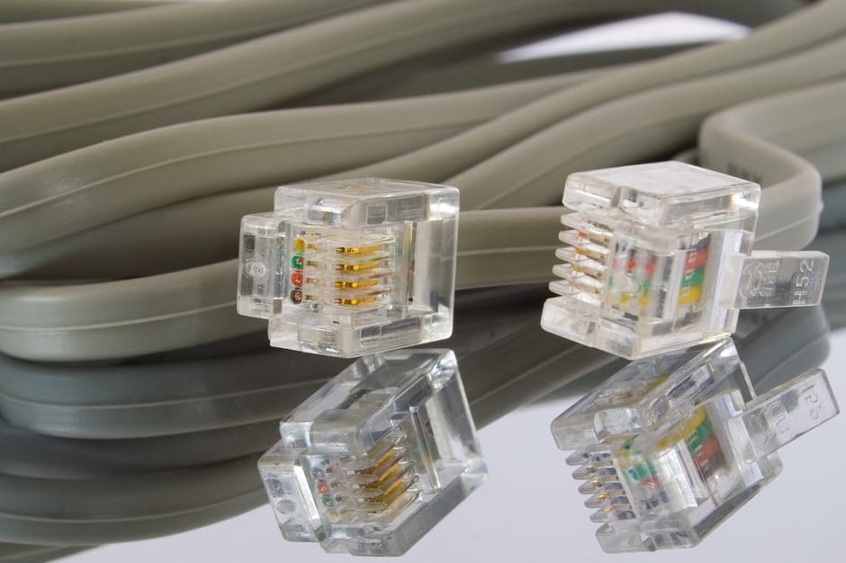 Close-up of several clear plastic Ethernet cables with gold-plated connectors, resting on a reflective surface. The cables are coiled and layered, with some connectors slightly elevated, revealing det